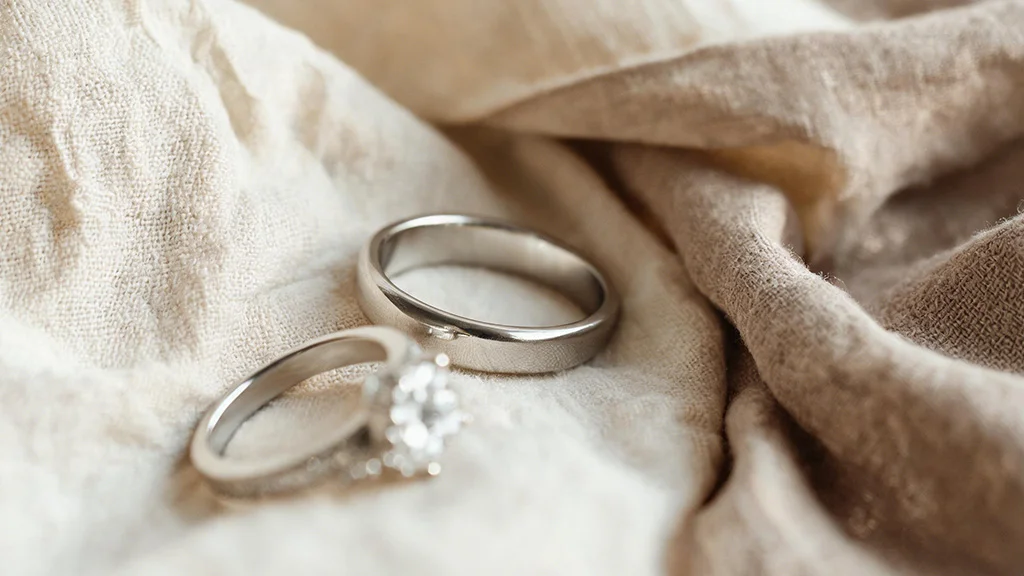 A white gold diamond ring and a sterling silver ring resting on linen fabric shown for comparison of white gold vs silver