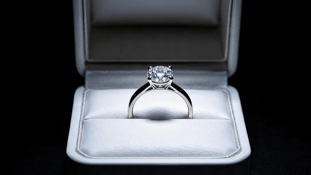 An open ring box presenting a brilliant diamond solitaire engagement ring