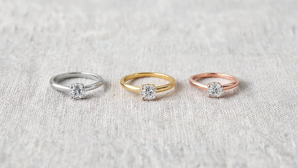 Three diamond solitaire rings in white gold, yellow gold, and rose gold