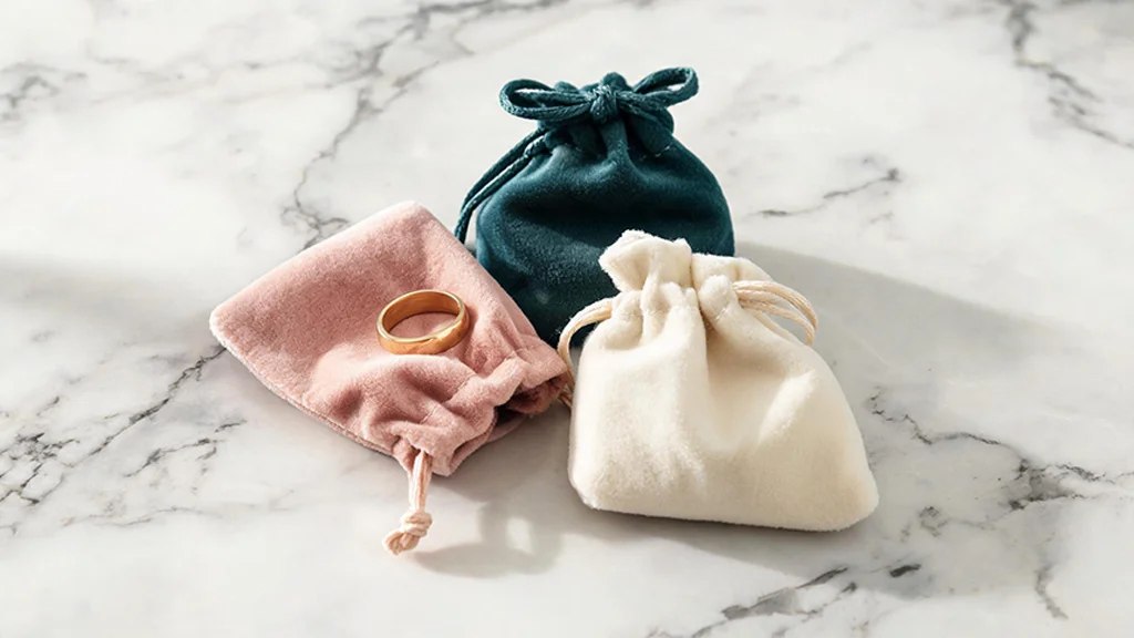 Velvet drawstring jewelry pouches in blush, teal, and cream with a ring inside one