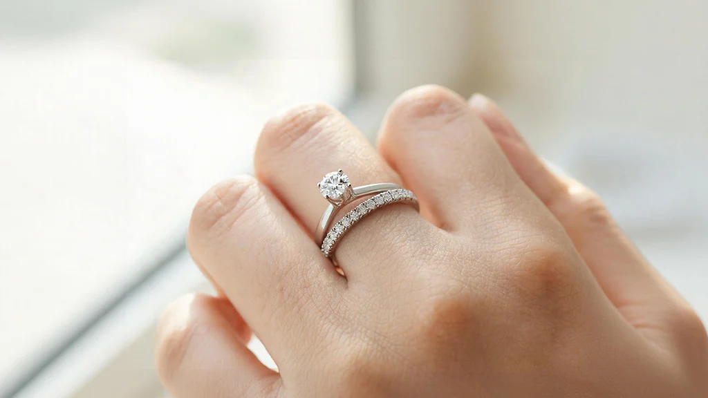 Woman's hand wearing a thin diamond pavé wedding band next to an engagement ring