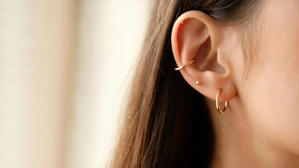 Woman wearing a layered gold earring stack with hoop, stud, and ear cuff